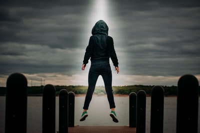 身穿黑色连帽衫和蓝色牛仔牛仔裤的男子站在灰色云层下的黑色金属栅栏上